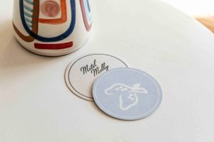 Branded coasters with geometric designs and bee logo on white surface.