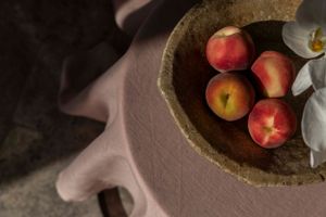 Fresh peaches in a rustic stone bowl against a dark background.