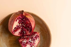 A ripe pomegranate cut in half reveals its vibrant red seeds on a rustic wooden surface.
