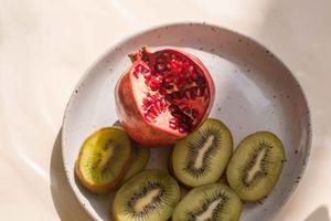 Fresh sliced kiwi and pomegranate arranged on a white ceramic plate for a healthy breakfast presentation.