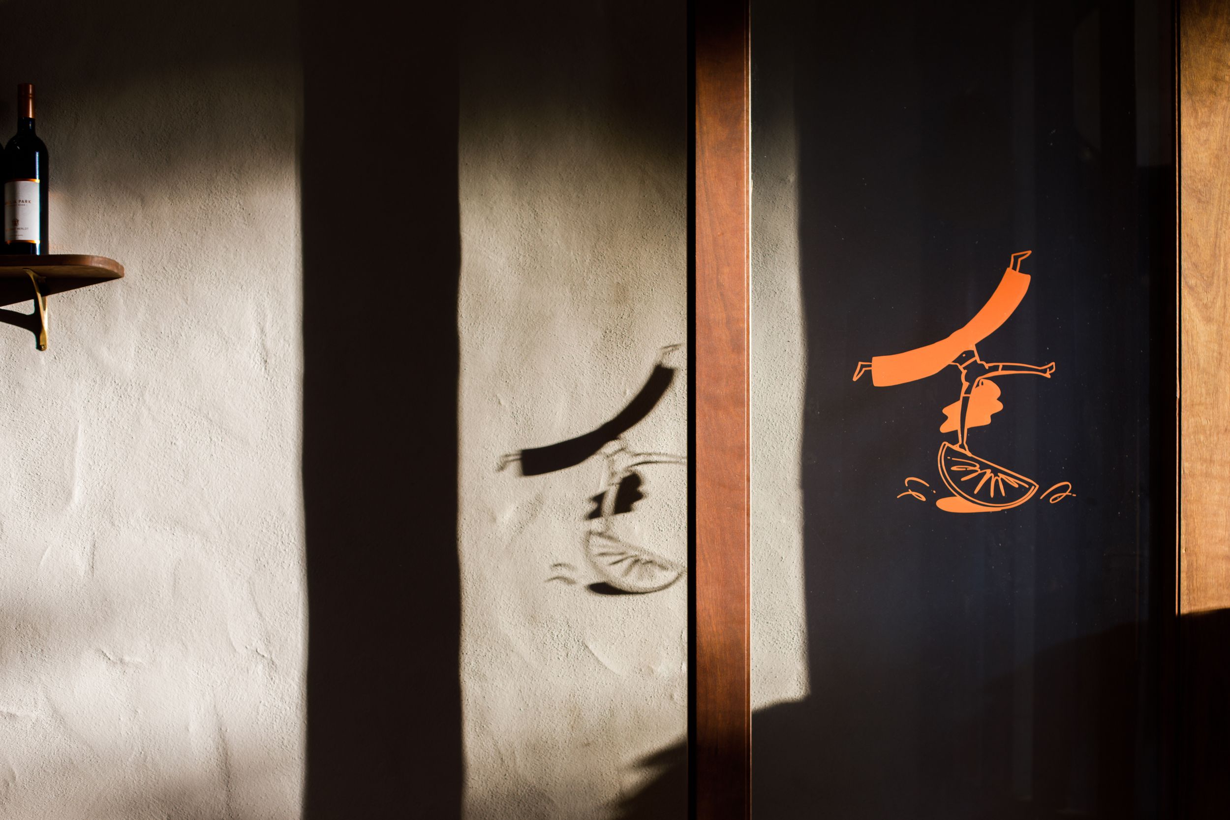 Sunlit wall with orange Japanese logo on dark panel and shadow art in rustic interior.