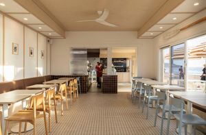 A modern cafe interior with mixed seating featuring wood chairs, tiled floors, and warm lighting with large windows.