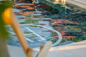 Close-up of a swimming pool edge with colorful reflections on rippling water and a white depth marker on the tiled floor.