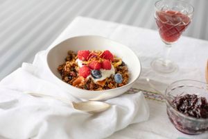 Breakfast bowl with granola, berries and yogurt served with red wine on white tablecloth.