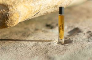 Small amber glass roller bottle with essential oil photographed on textured stone surface in natural lighting.