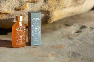 Orange glass bottle and gray box with Sisuu branding displayed against stone background.