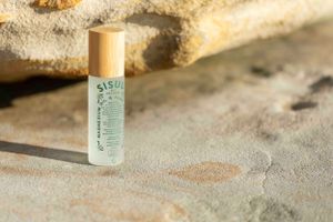 Clear glass bottle with light green liquid displayed on rough stone surface in soft lighting.