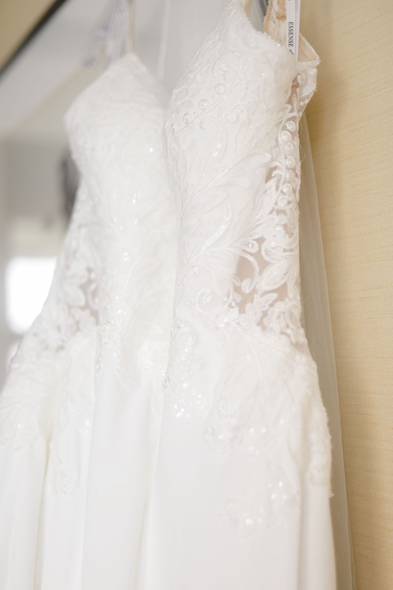 Close-up detail of delicate lace and beading on a hanging white wedding dress.