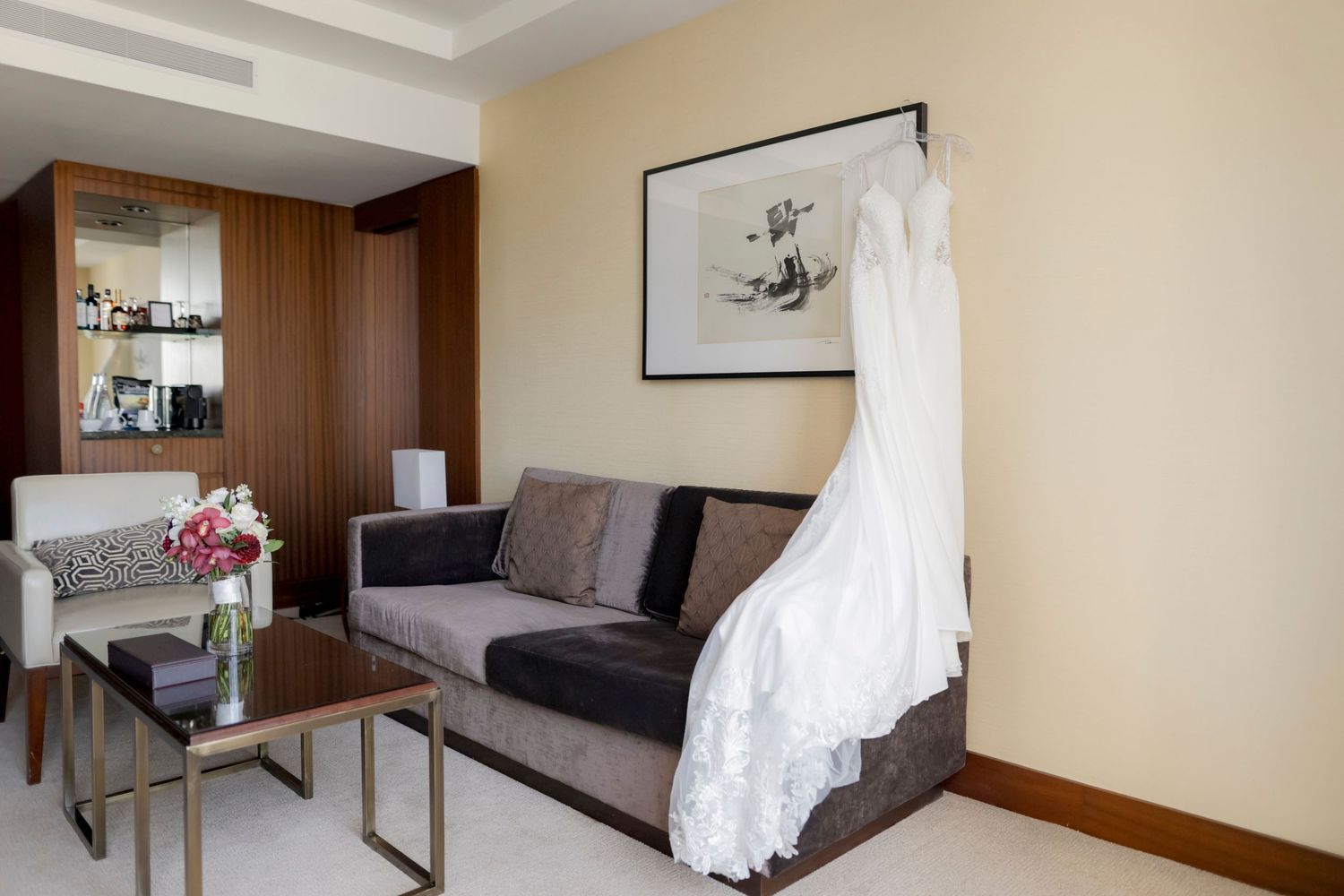 Modern living room interior featuring hanging wedding dress, gray couch and wooden furniture.