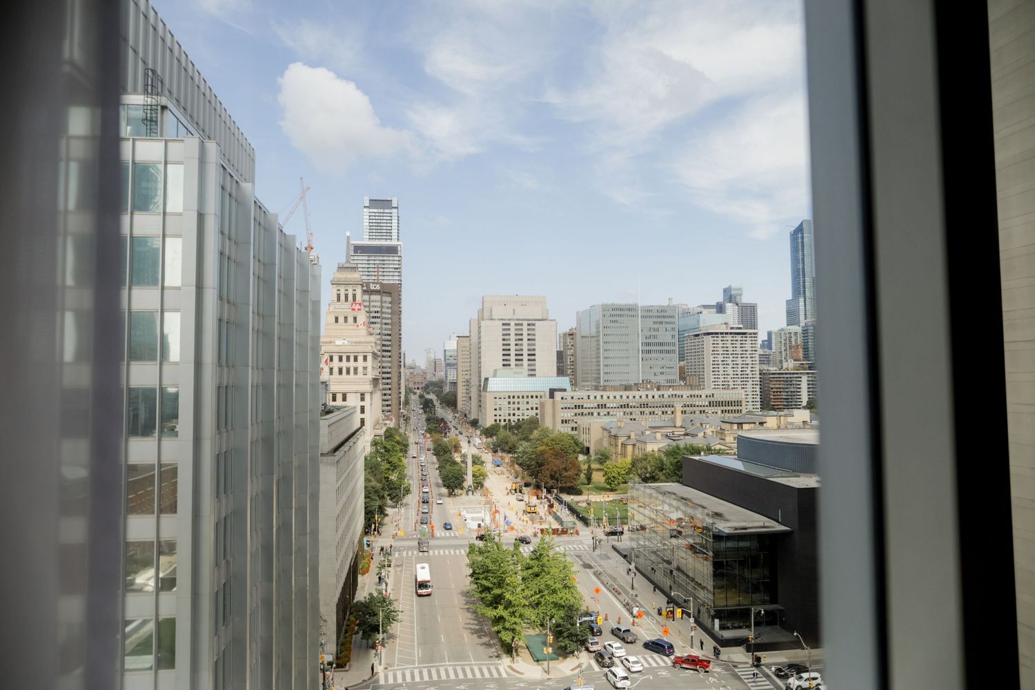 Aerial view of a downtown cityscape with modern buildings and tree-lined streets on a sunny day.
