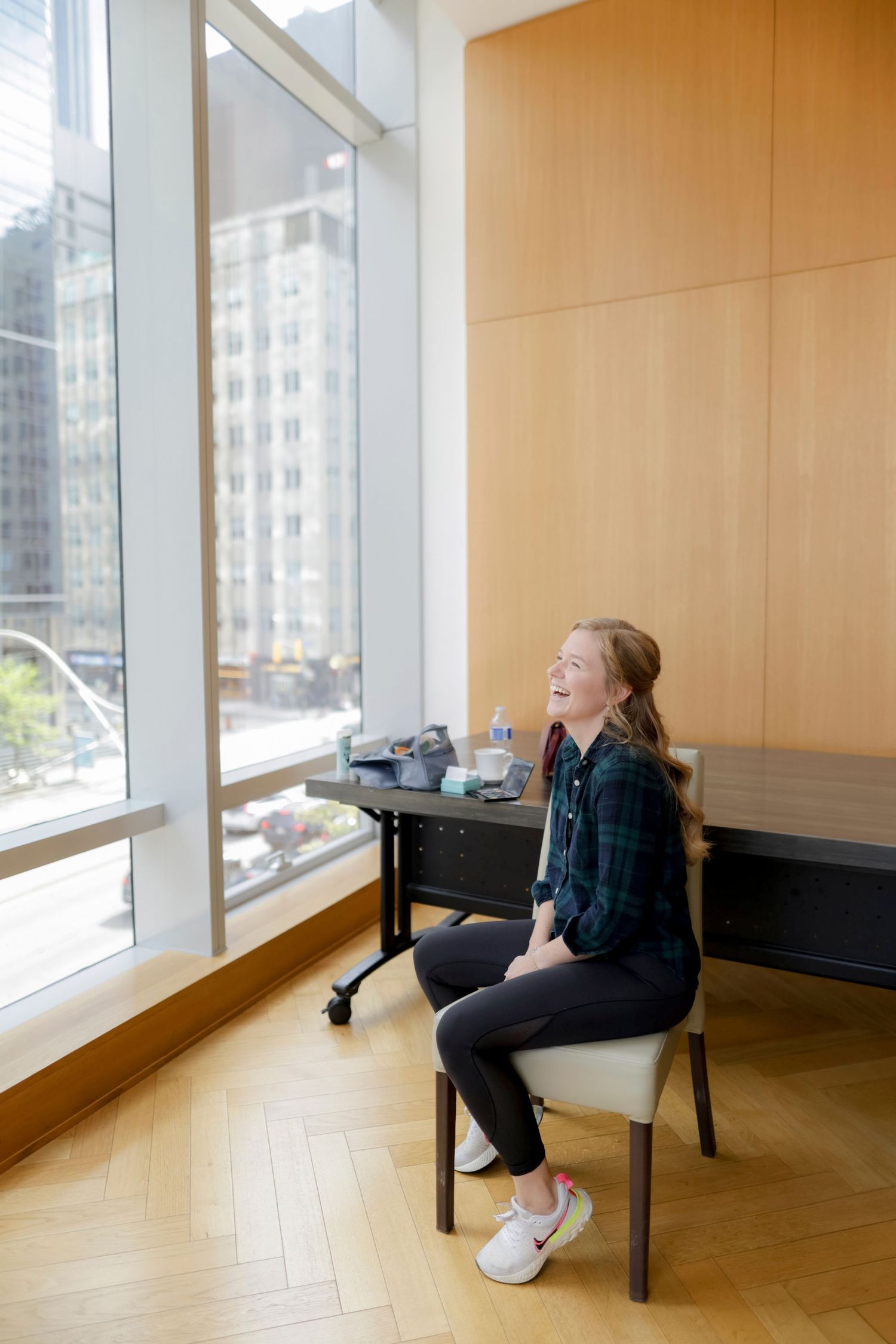 Person sitting by large windows in modern office space with city view.