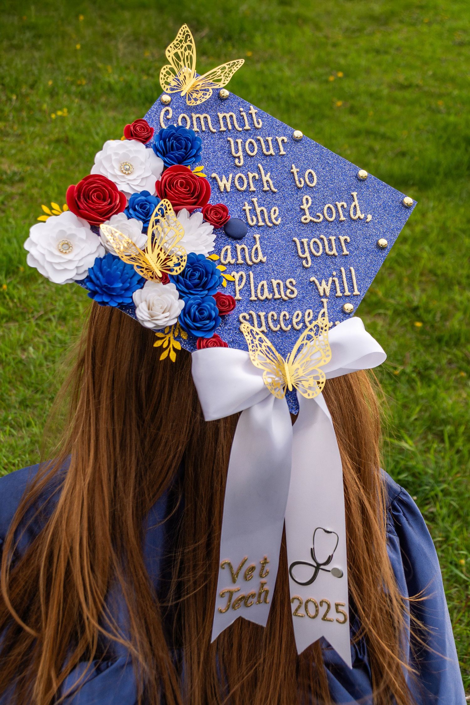 Decorated graduation cap with blue roses and religious quote in gold lettering.