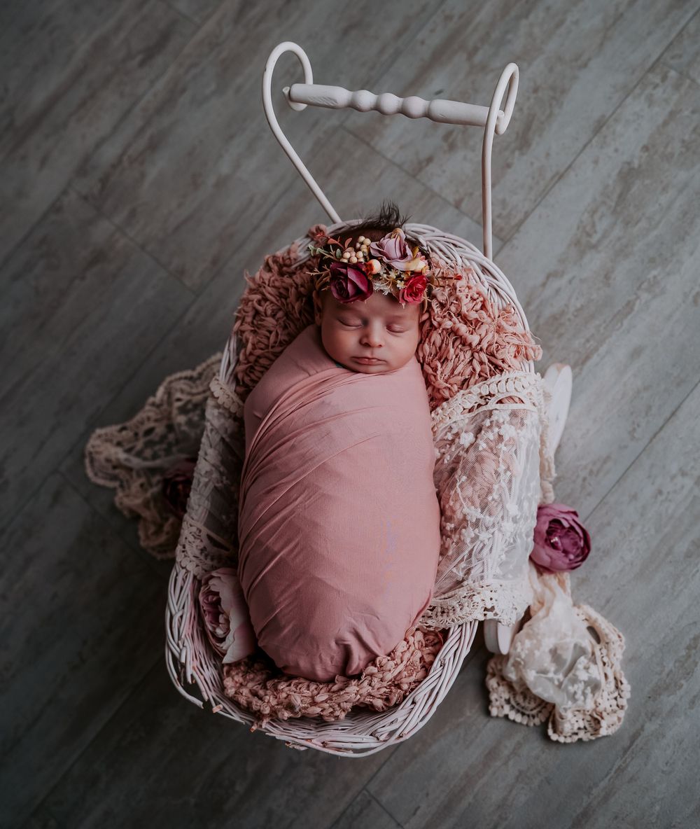 Newborn photography composition featuring pink wrap and delicate lace in rustic setting.