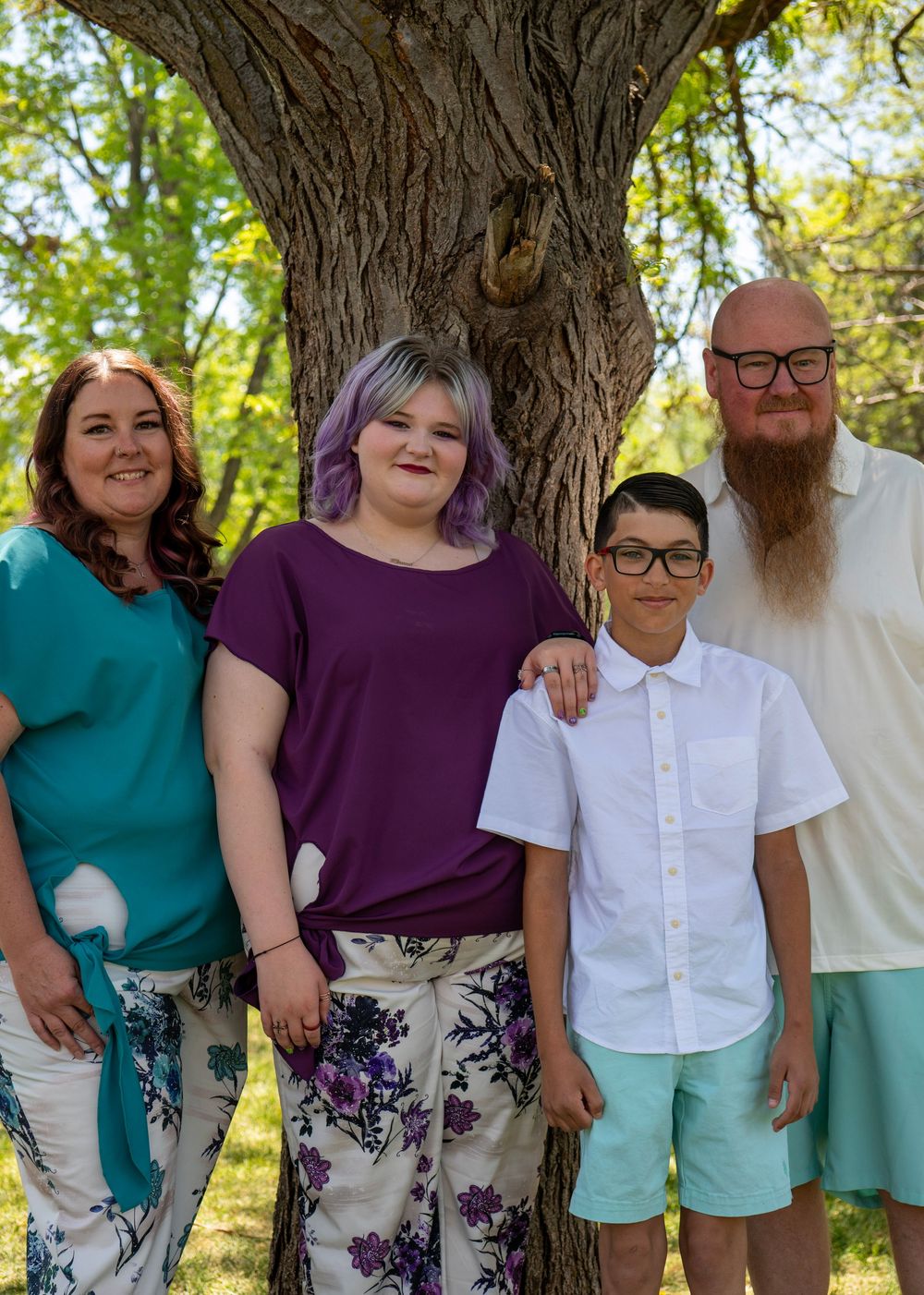 Family of four posing outdoors near a large tree, dressed in coordinated outfits for a portrait session.