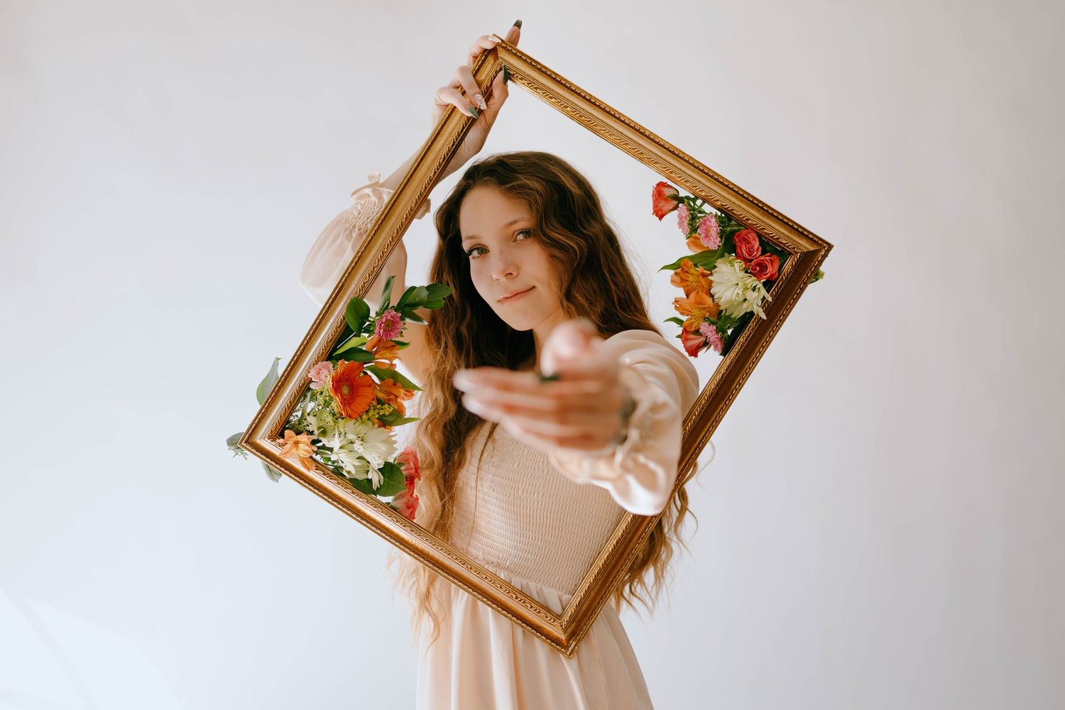Person holding decorative gold frame with floral elements against white background.