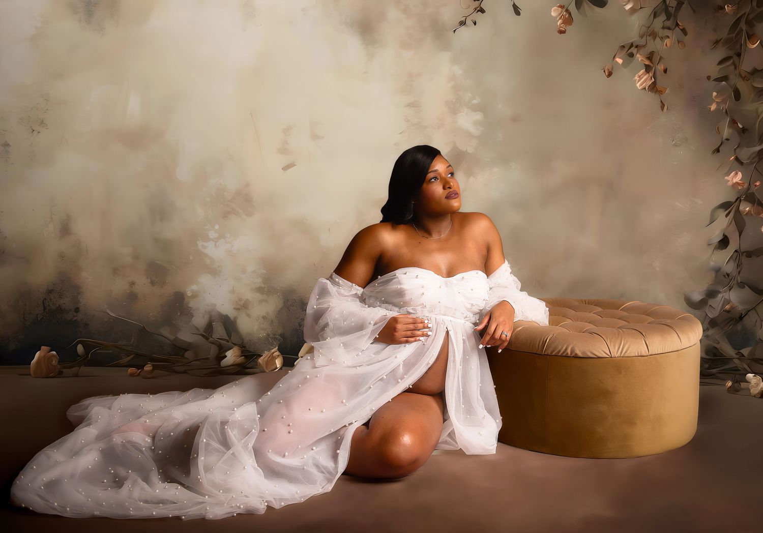 Artistic maternity boudoir photo with white lace robe and vintage ottoman.
