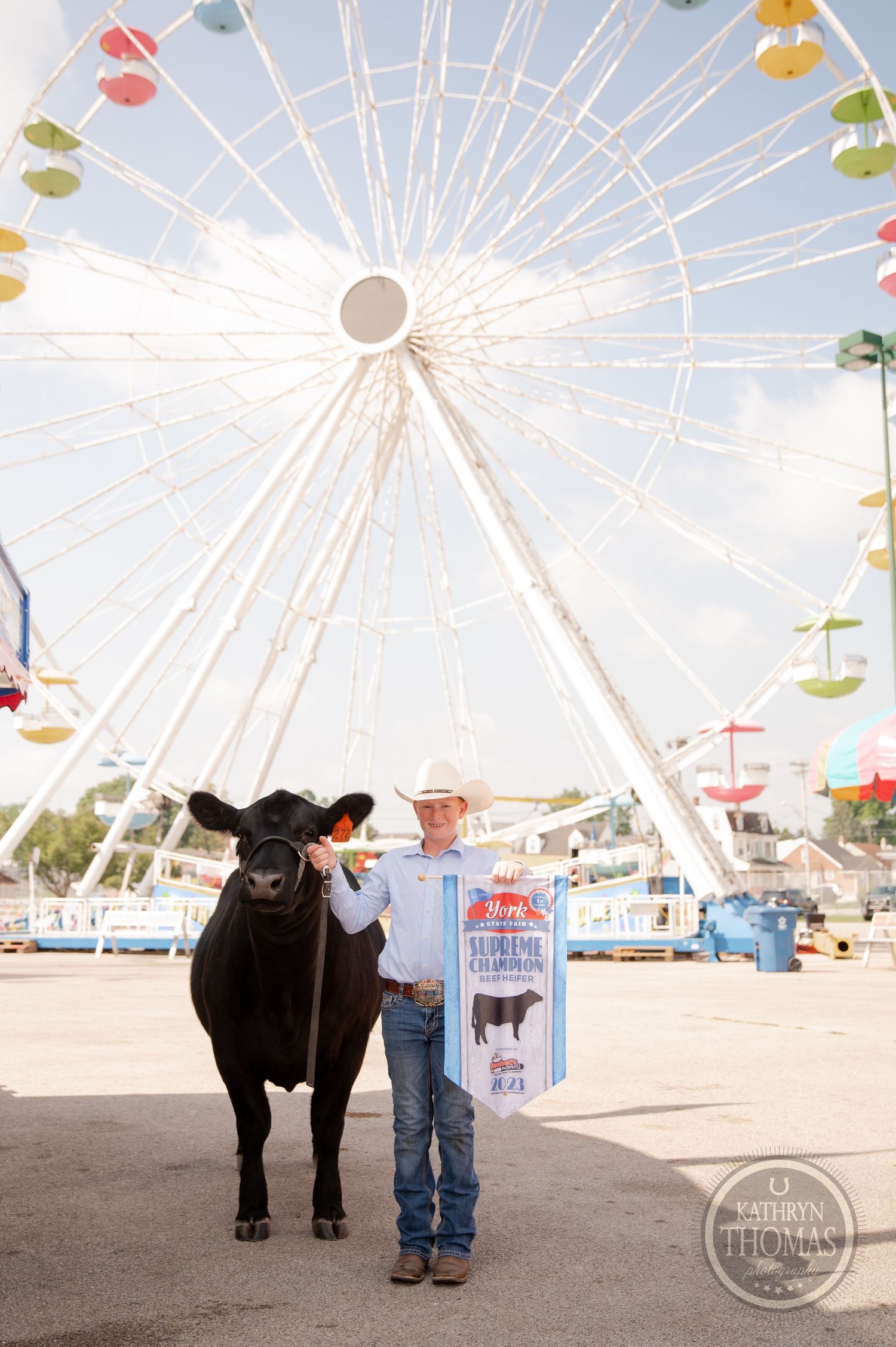 A black show animal poses with an award banner in front of a large Ferris wheel at a fairground.