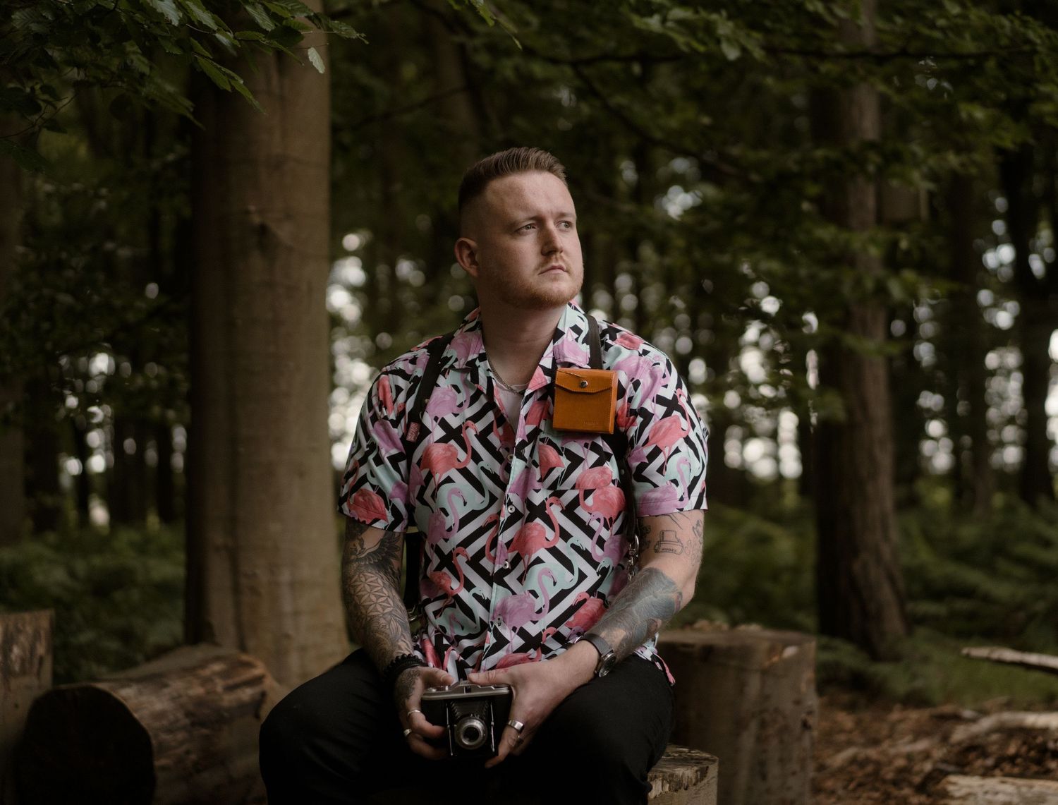 A portrait in the woods features someone wearing a bold geometric print shirt while holding a camera.