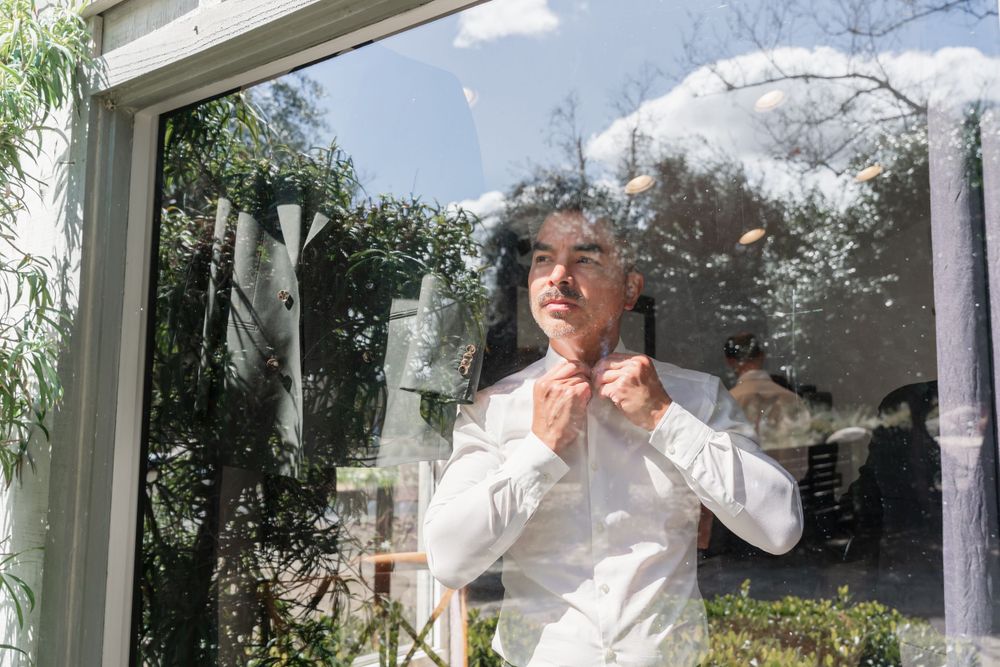 Preparing for formal event by adjusting bow tie near bright window.