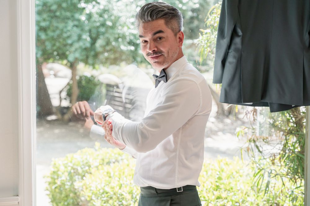 Getting dressed in formal attire with white shirt and bow tie by window.