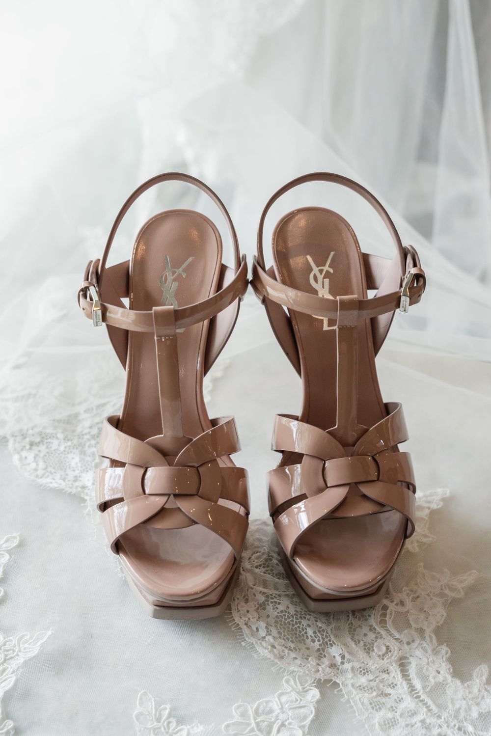 YSL nude platform sandals with crossed straps placed on white lace fabric.