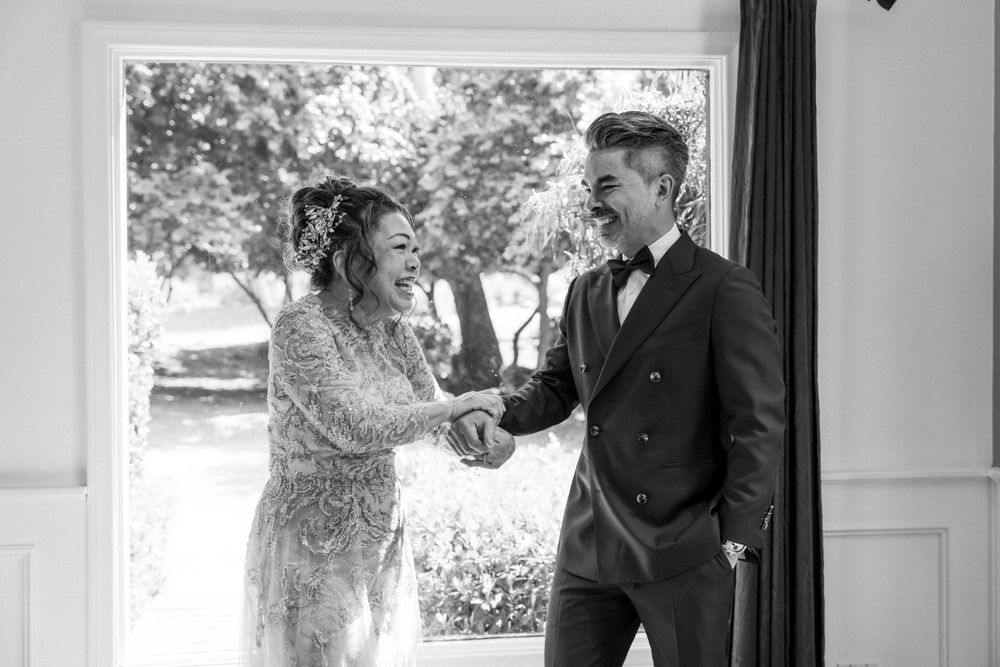 Joyful wedding moment captured in black and white by window.