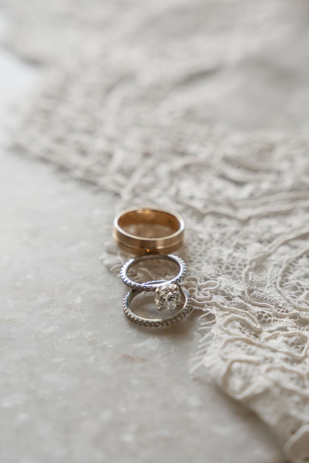 Wedding rings with diamonds resting on white lace fabric in soft focus.