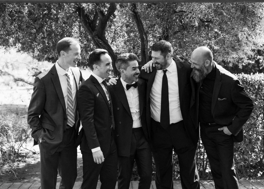 A casual black and white group photo of five men in suits standing together outdoors.