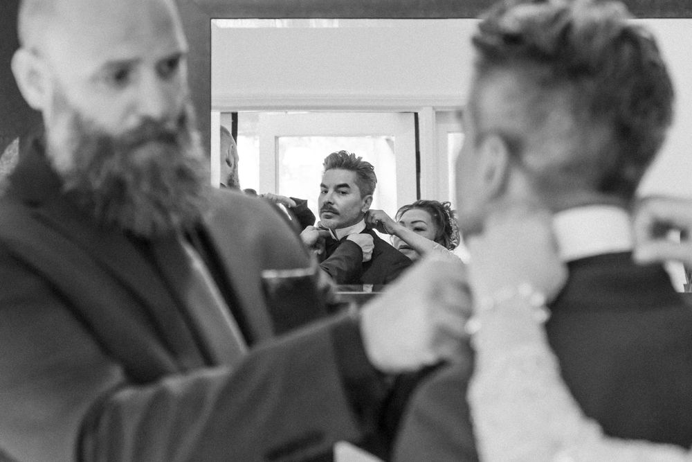 A black and white candid photo of groomsmen getting ready before a wedding ceremony.