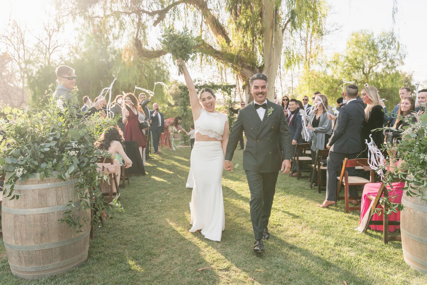 Newlyweds walking down the aisle at outdoor garden ceremony during golden hour.