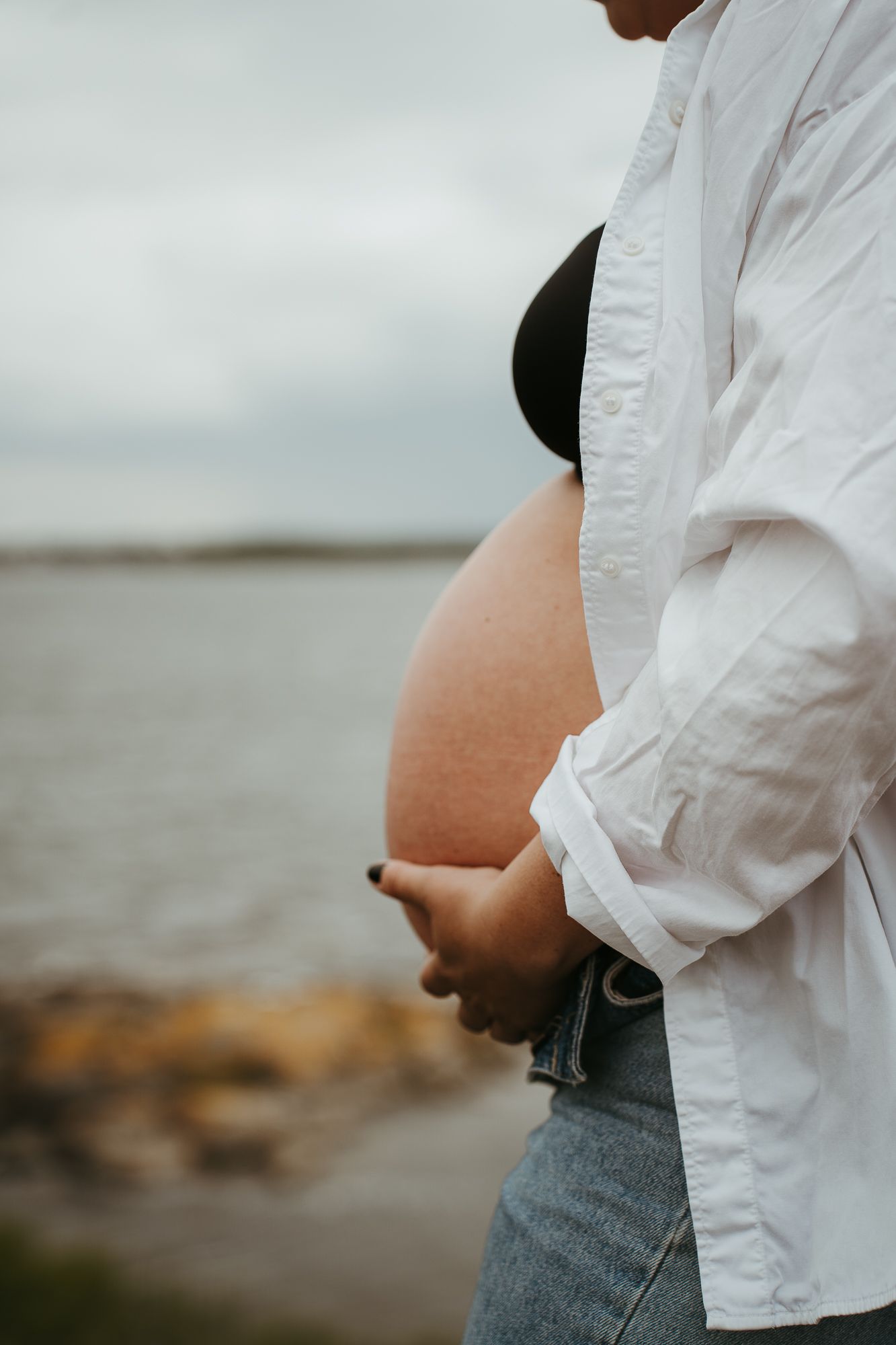 Side view of a pregnant belly against an overcast ocean backdrop.