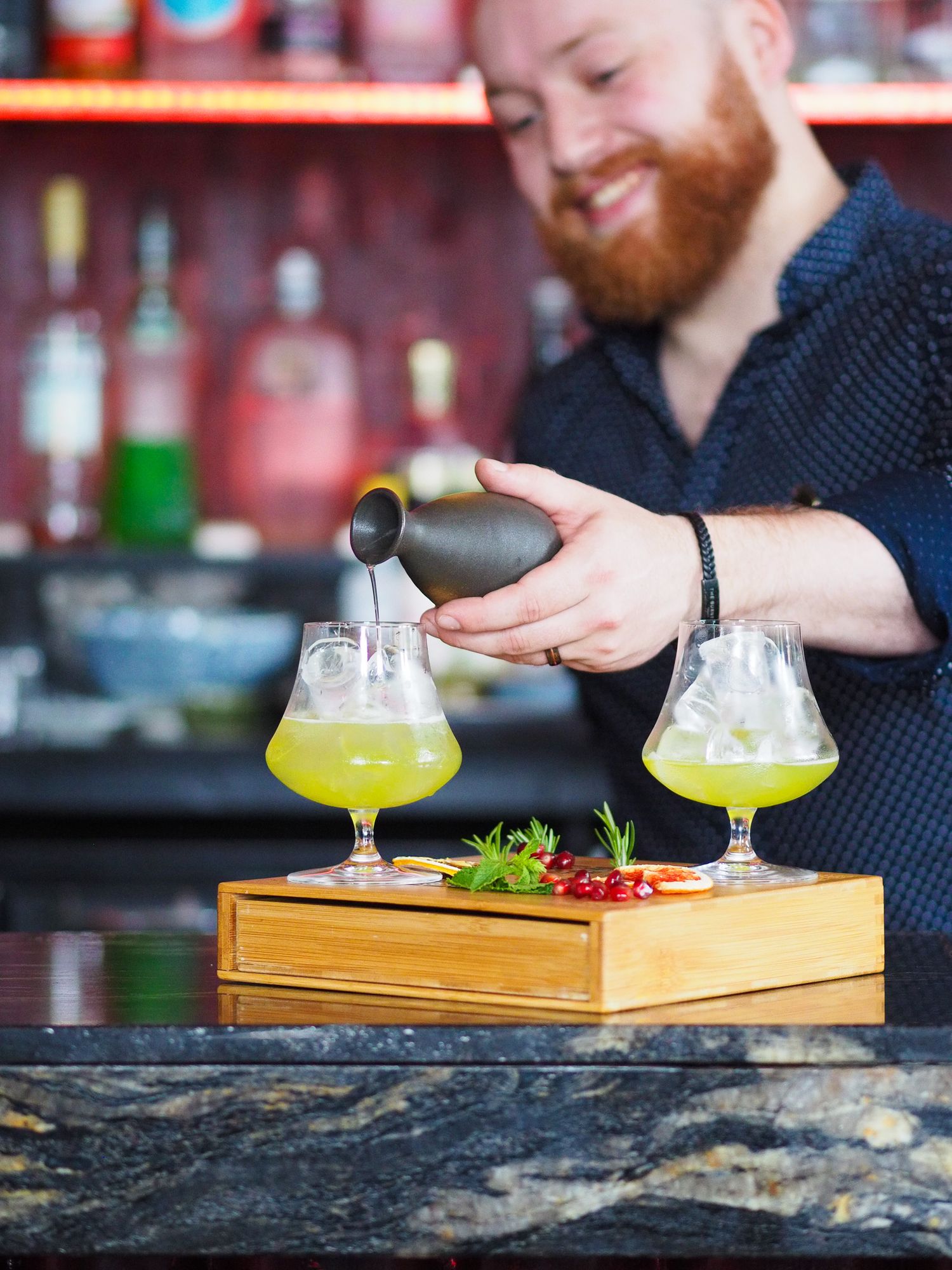 Bartender pours creative cocktails on a wooden serving board with fresh garnishes.