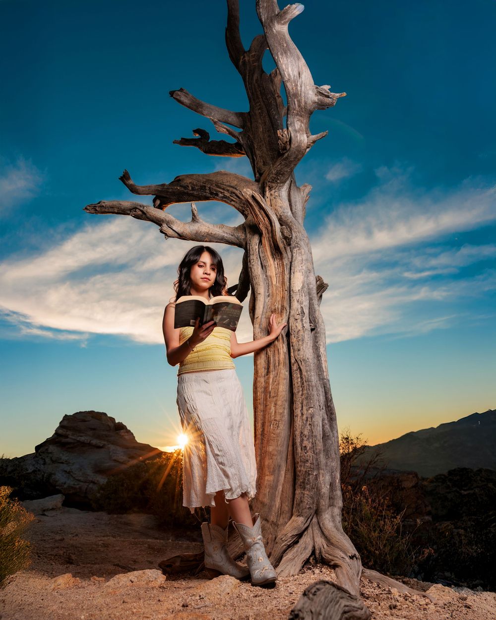 senior girl reading a book leaning on a tree on Mt. Lemmon with mountain views and a sun burst