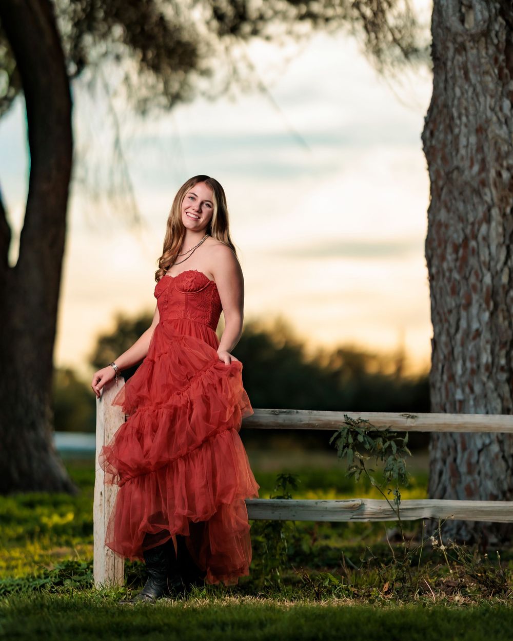 senior girl in rust colored dress and boots under a tree and wood fence golden hour Tucson, AZ