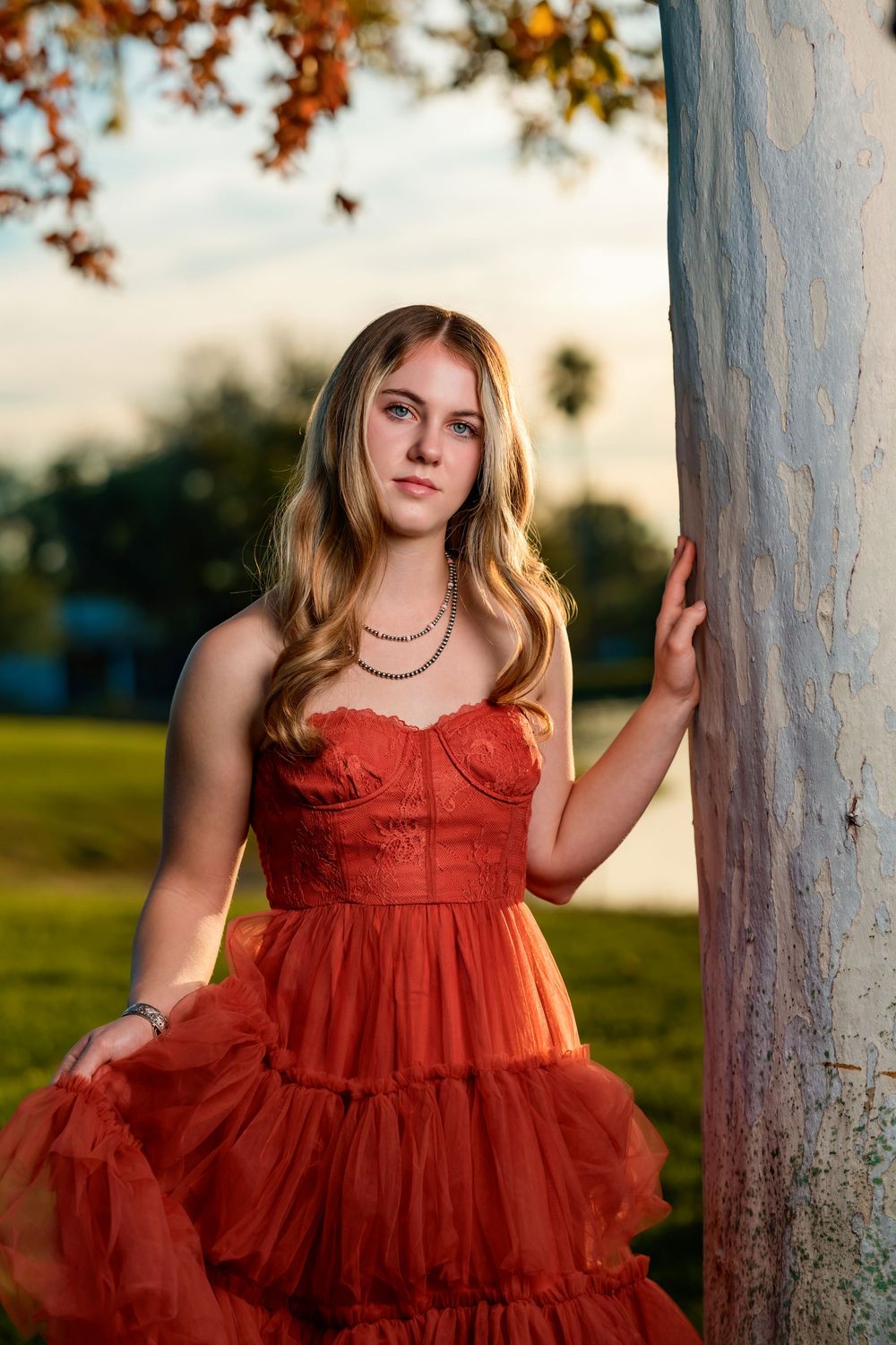 senior girl in rust colored dress and boots under a tree with fall leaves Tucson, AZ
