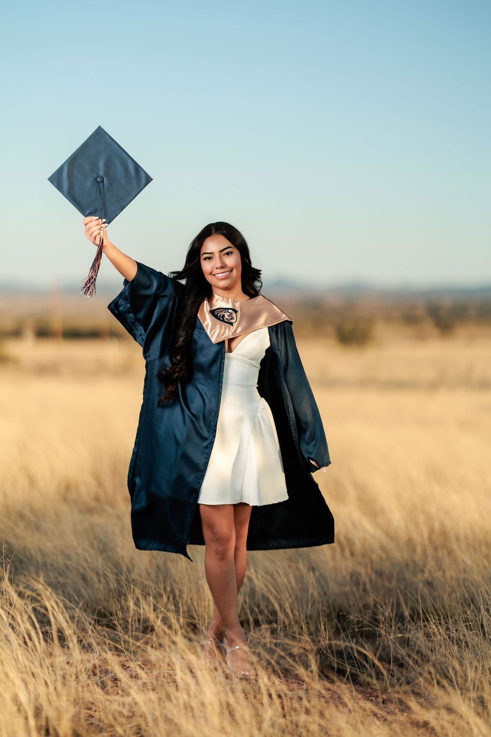 Tucson, AZ senior girl in a field at golden hour with a white dress and cap and gown