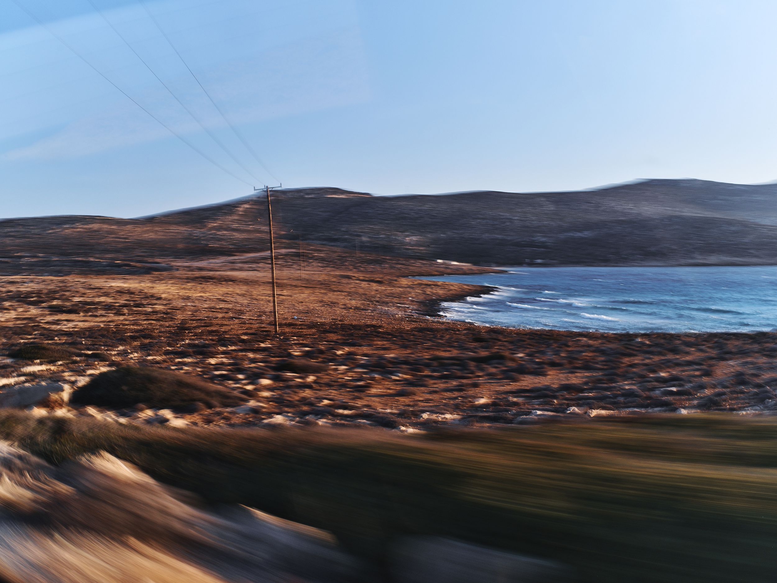 Panoramic coastal landscape with rolling hills and curved shoreline at sunset.