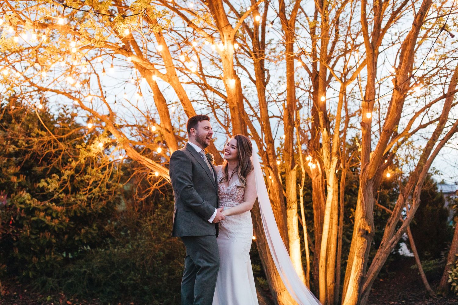 Golden sunset wedding portrait with couple standing among fall-colored trees.