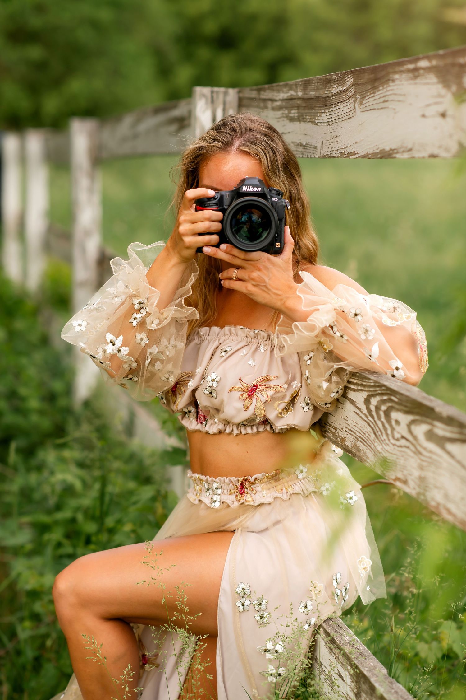 Photographer wearing blue dress holding professional camera in sunlit field.