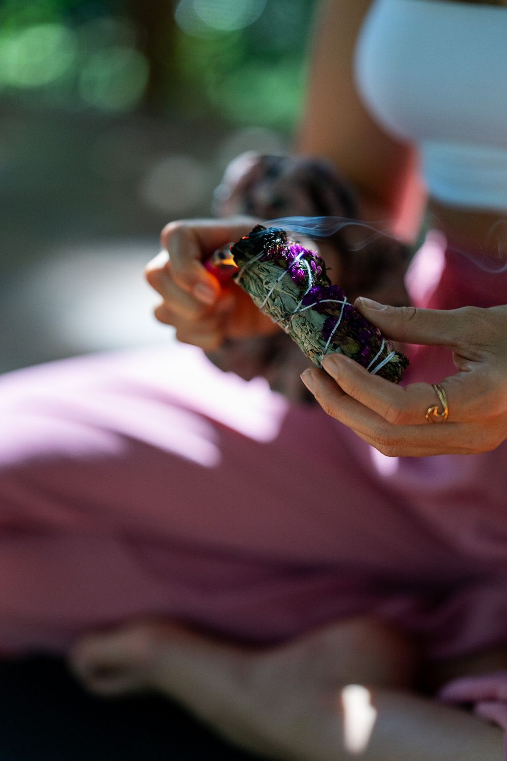 Close-up of hands holding an iridescent crystal in sunlight with pink fabric visible.