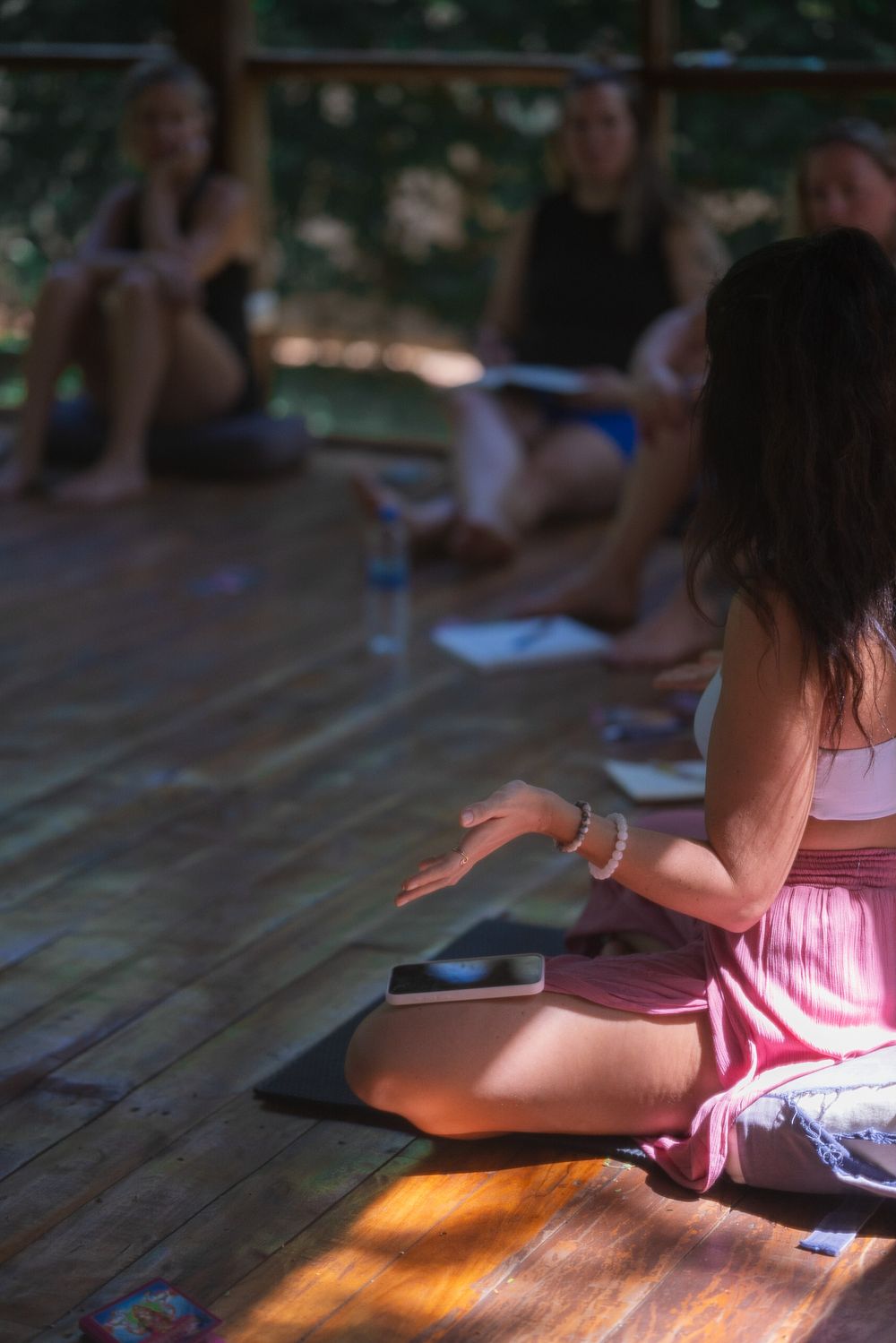 Person sitting cross-legged on wooden deck during outdoor meditation session.