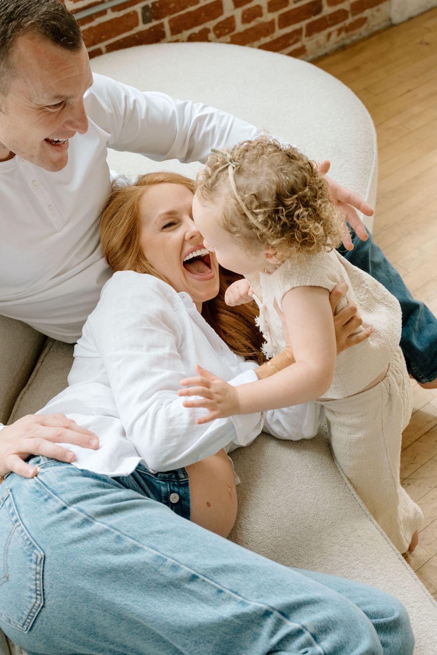Intimate moment between parent and child sitting on white furniture in casual clothing during maternity photoshoot in San Diego.