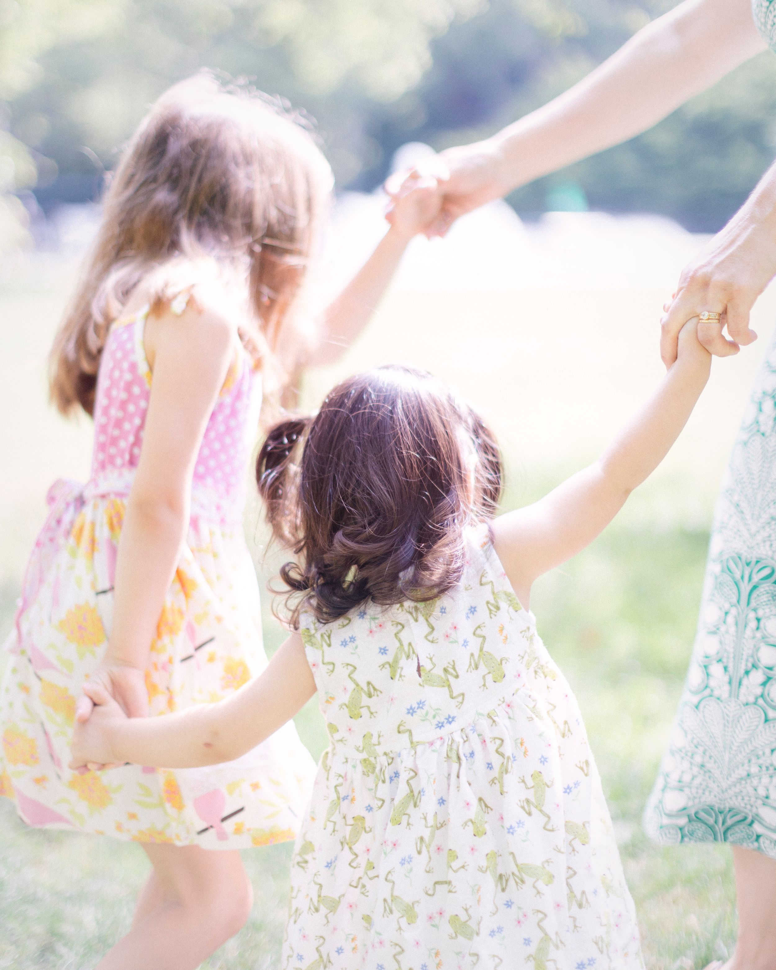 Children in summer dresses holding hands while dancing in sunlit garden.