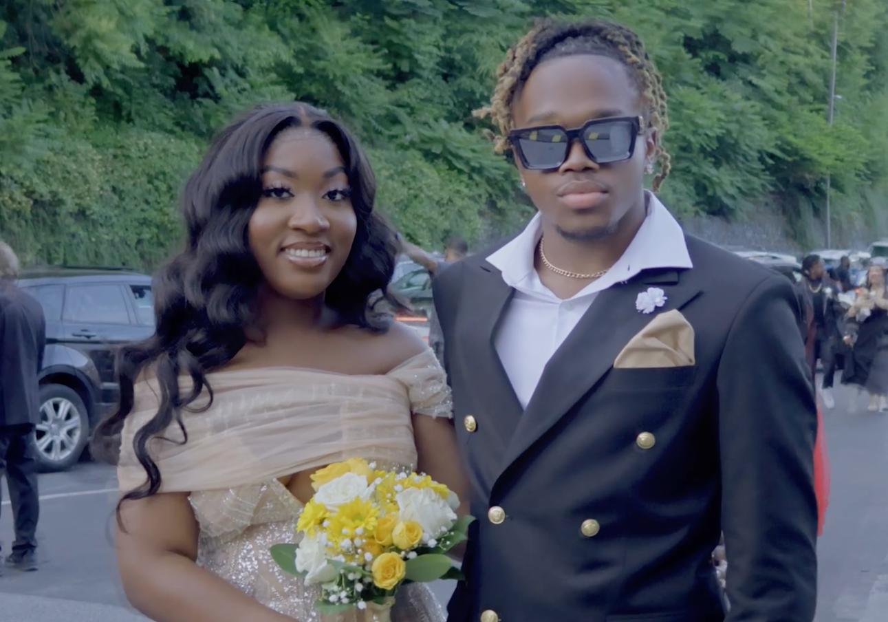 Couple in formal attire holding yellow flowers at outdoor celebration.