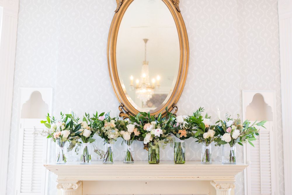 Elegant gold oval mirror above a white mantle decorated with floral arrangements.