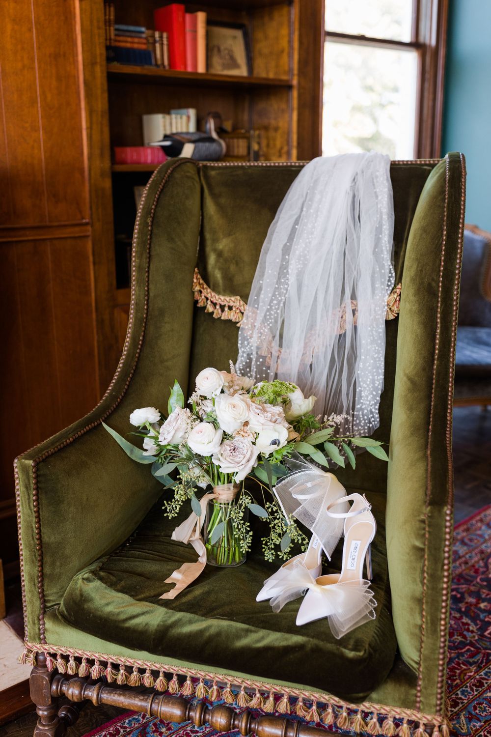 Wedding accessories displayed on green velvet chair including bouquet, veil, and white shoes.