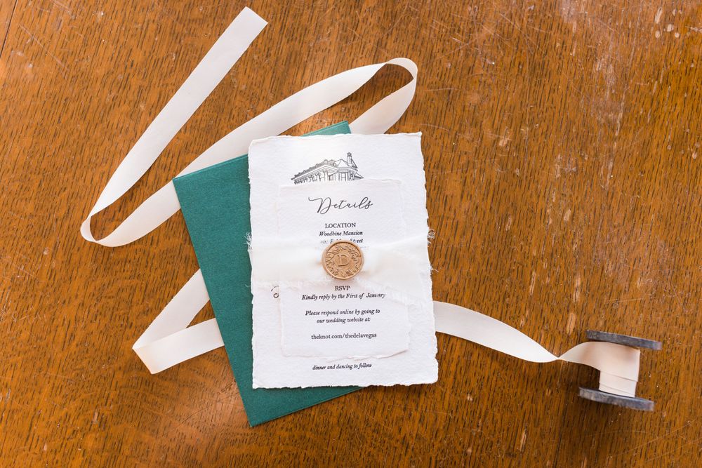 Wedding invitation suite with white and green paper elements on wooden surface.