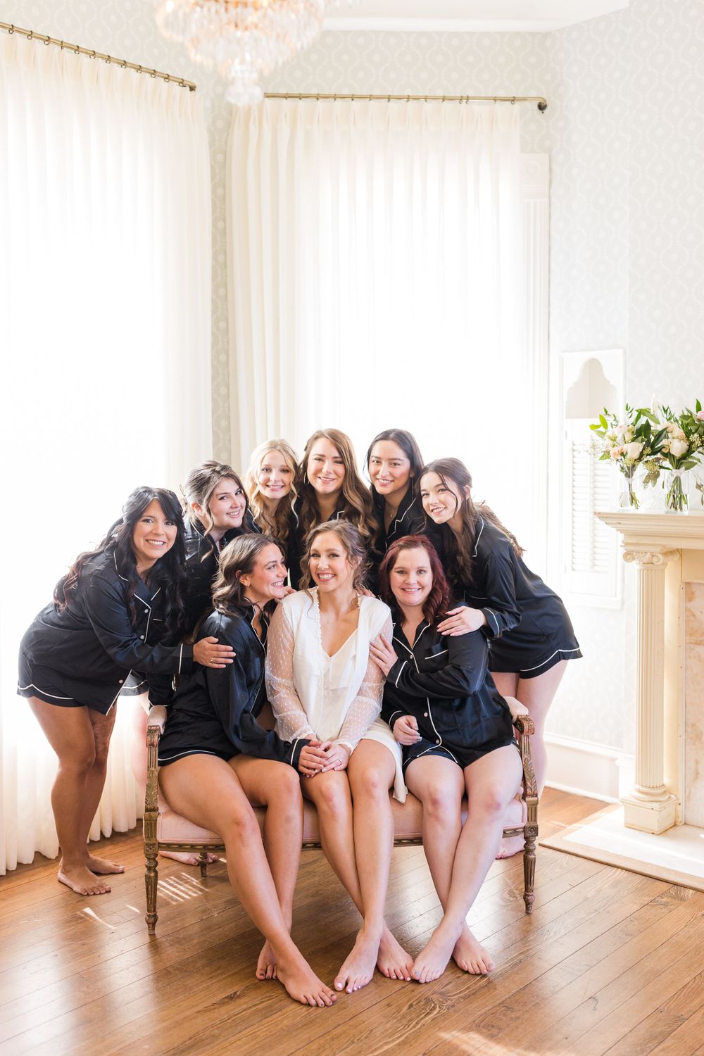 Wedding party wearing matching black robes poses together in a bright room.