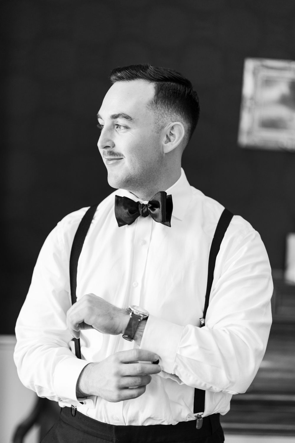 Classic black and white portrait of a groom in suspenders and bow tie.