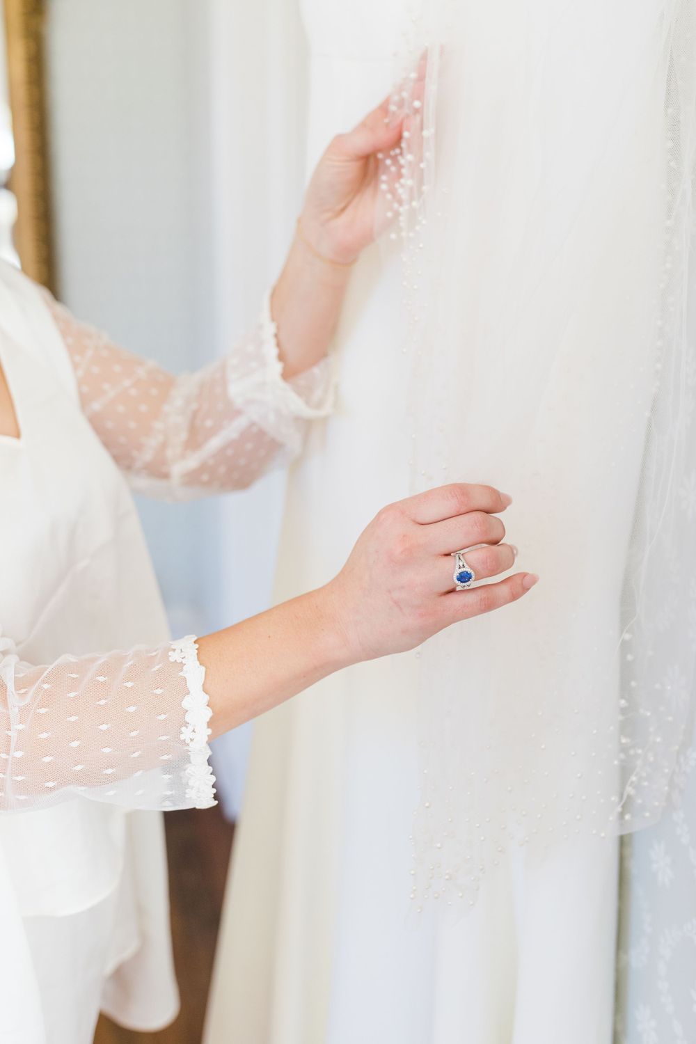 Close-up of lace sleeve and engagement ring details on a wedding dress.